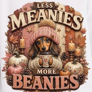 May include: A white sweatshirt featuring a dachshund wearing a pink beanie and holding a mug. The image includes the text "LESS MEANIES MORE BEANIES" with fall-themed decorations like pumpkins, candles, and leaves.