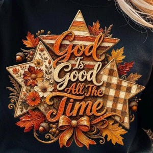 May include: A black sweatshirt featuring a graphic of three layered stars decorated with autumn leaves, acorns, and flowers. The text "God Is Good All The Time" is printed in orange script across the stars, accented by a bow at the bottom.