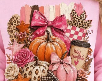 May include: Pink sweatshirt featuring a fall-themed graphic. The design includes pumpkins, bows, stars, and floral elements. The graphic also has a coffee cup with the text "hey pumpkin" and a heart.