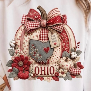 May include: A white sweatshirt featuring a large graphic of a pumpkin decorated with red and white patterns, a bow, and a tag reading Home Sweet Home. A gray map of Ohio with a red heart is centered on the pumpkin, with the word OHIO printed below.