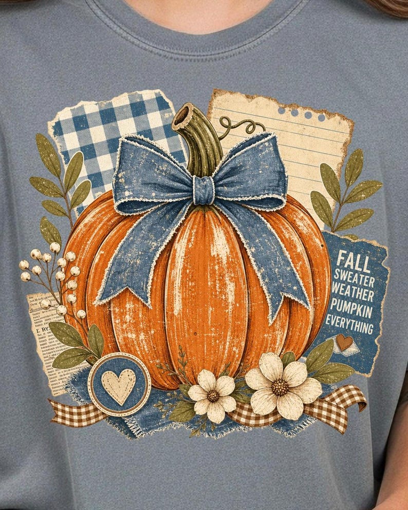 May include: A light blue t-shirt featuring a large orange pumpkin with a blue bow. The design includes floral accents, a heart, and the text "FALL SWEATER WEATHER PUMPKIN EVERYTHING" on a blue background.