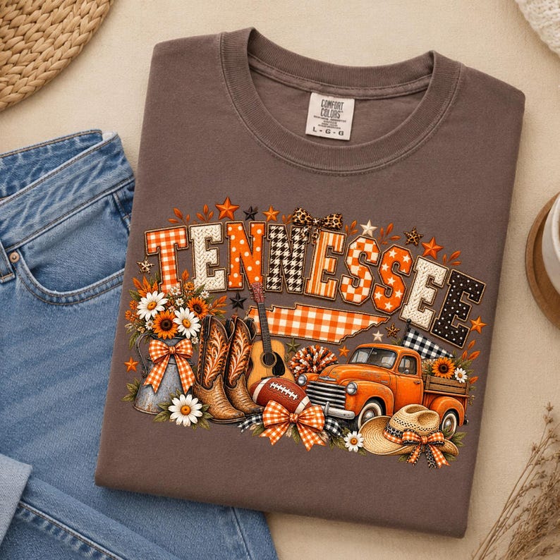 Może przedstawiać: Brązowy t-shirt z grafiką przedstawiającą napis TENNESSEE w pomarańczowo-białe wzory. Projekt zawiera zarys stanu, parę kowbojek, gitarę akustyczną, piłkę do futbolu amerykańskiego, pomarańczowy pickup oraz kowbojski kapelusz.