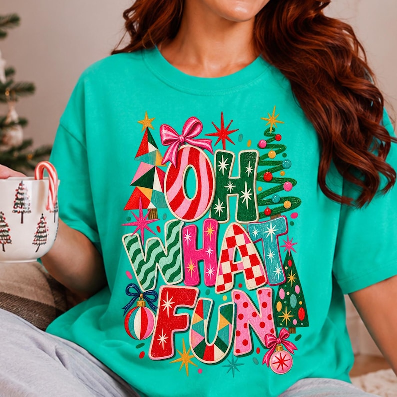 K&ouml;nnte beinhalten: Ein leuchtend t&uuml;rkisfarbenes T-Shirt mit einem bunten Grafikdruck und dem Text "OH WHAT FUN" in stilisierten, gemusterten Buchstaben. Das Design zeigt Weihnachtsb&auml;ume, Christbaumkugeln, eine rosa Schleife und sternf&ouml;rmige Motive.