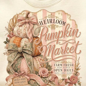 Puede incluir: Una camiseta blanca con un diseño de temática otoñal. El diseño incluye calabazas apiladas con patrones florales y lazos, junto con el texto "Heirloom Pumpkin Market". El texto adicional dice "Locally Grown Autumn Harvest" y "Farm Fresh Open Daily."