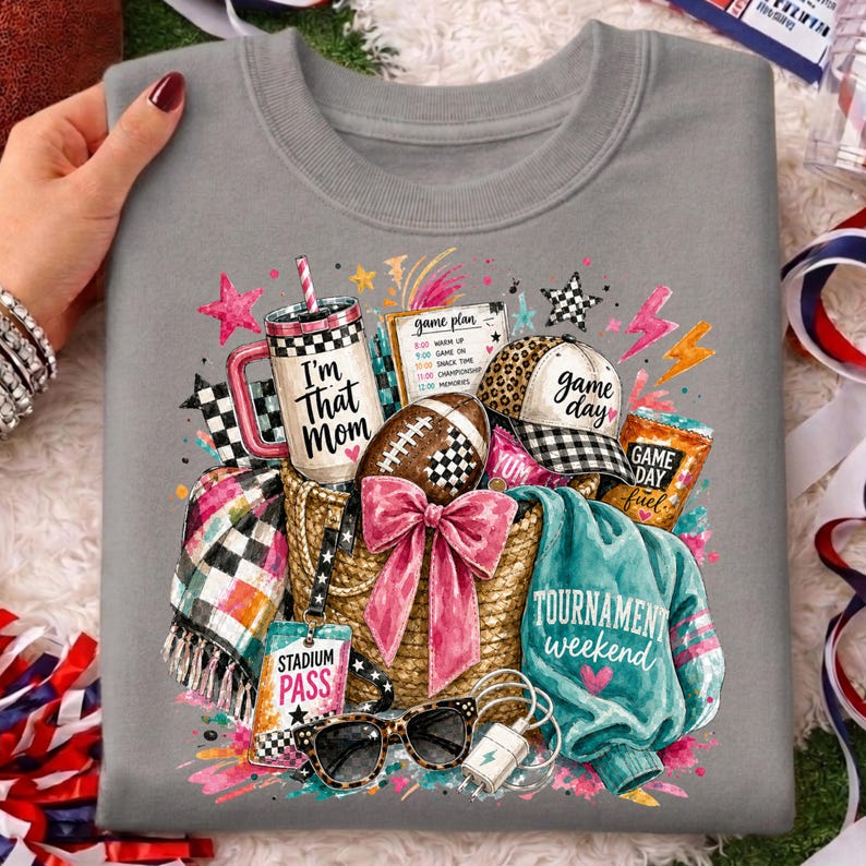 May include: A grey crewneck sweatshirt featuring a graphic print of a straw tote bag filled with a tumbler labeled 'I'm That Mom', a football, a leopard print cap, a teal sweater, a plaid blanket, sunglasses, and a stadium pass.