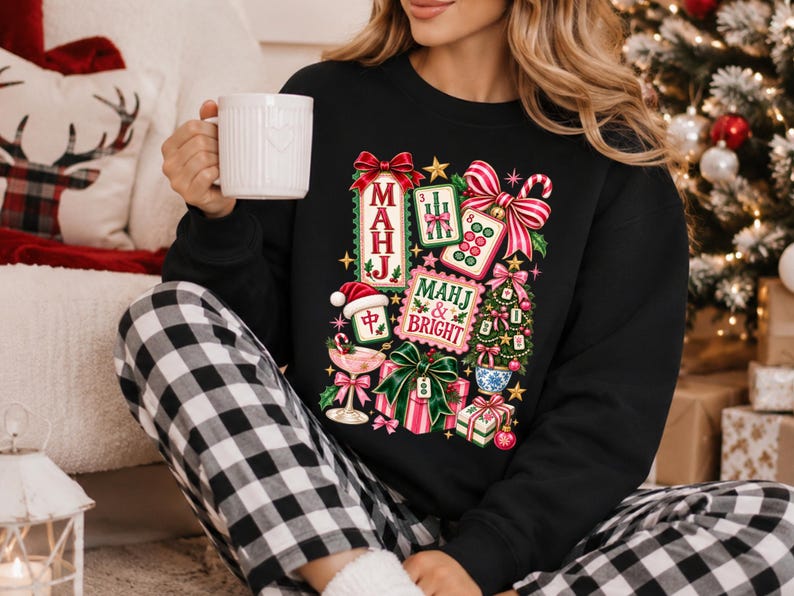 K&ouml;nnte beinhalten: Ein schwarzes Langarm-Sweatshirt mit einem bunten Grafikdruck aus Mahjong-Steinen, einem Weihnachtsbaum, verpackten Geschenken, einer Zuckerstange und einem Cocktailglas. Der Text lautet MAHJ und MAHJ & BRIGHT in festlichen roten und gr&uuml;nen Buchstaben.