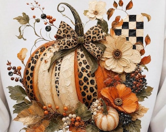 May include: A white sweatshirt featuring a graphic print of a large pumpkin decorated with a leopard print bow, surrounded by orange and white flowers, dark berries, green leaves, and a black and white checkered pattern element.