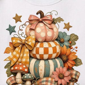May include: A stacked pumpkin design with a pink polka-dot pumpkin, orange and white checkered pumpkin, and a blue and white striped pumpkin. The design includes orange and yellow bows, flowers, mushrooms, and stars. A plaid ribbon is at the bottom.