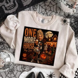 Puede incluir: Una sudadera de cuello redondo color crema con un estampado gr&aacute;fico de una persona con una camiseta de fantasmas, sosteniendo una bebida y un cubo de calabaza. El texto dice ONE MORE HOUSE They Said... con una casa embrujada de fondo.