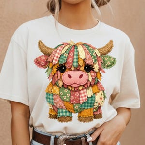 Puede incluir: Camiseta color crema con un diseño de vaca de las Highlands en patchwork colorido. La vaca tiene ojos grandes, nariz rosa y cuernos marrones. El patchwork incluye patrones florales, a cuadros y lisos en varios colores. Una prenda casual.