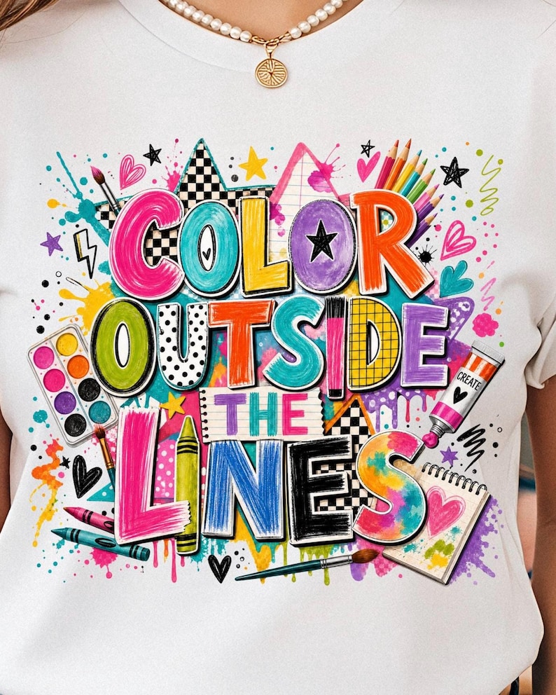 May include: A white t-shirt featuring a colorful graphic with the text "COLOR OUTSIDE THE LINES". The design includes illustrations of paintbrushes, a watercolor palette, crayons, a paint tube, and a sketchbook, surrounded by paint splatters.