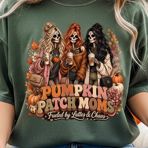 May include: Green t-shirt featuring a graphic of three skeleton women with long hair, holding coffee cups, and wearing fall-themed outfits. The text "PUMPKIN PATCH MOMS" and "Fueled by Lattes & Chaos" are also displayed.
