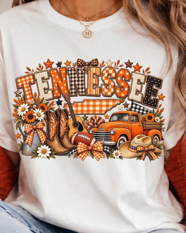 Może przedstawiać: Biały t-shirt z nadrukiem graficznym przedstawiającym słowo TENNESSEE w pomarańczowe i czarne wzory. Projekt zawiera mapę stanu, pomarańczowy pickup, brązowe kowbojki, gitarę akustyczną, piłkę do futbolu amerykańskiego oraz słoneczniki.