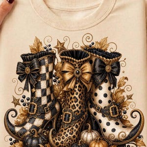 May include: A beige crewneck sweatshirt featuring a graphic print of three ornate, curled-toe boots. The boots display black and white checkered, leopard print, and polka dot patterns, each adorned with a large bow, buckle, and gold leaf accents.