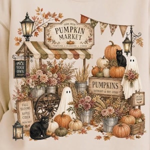 May include: A beige sweatshirt featuring a detailed graphic of a pumpkin market. The design includes pumpkins, flowers, black cats, ghosts, lanterns, and signs reading "Farm Fresh Pumpkin Market," "Pick Your Own," and "Fall Blooms Apple Cider."