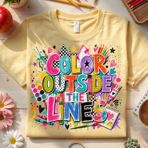 May include: A pale yellow short-sleeved t-shirt featuring a colorful graphic with the text "COLOR OUTSIDE THE LINES." The design includes illustrations of paint palettes, brushes, crayons, and a sketchbook surrounded by vibrant paint splatters.