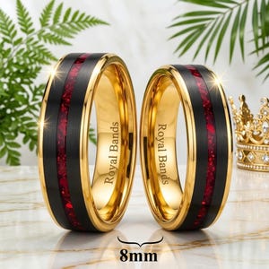 Puede incluir: Dos anillos con acabado negro cepillado e incrustación central de piedras rojas trituradas. Los bordes y el interior son de oro pulido. El texto Royal Bands está grabado en la superficie interior. Una etiqueta en la parte inferior indica 8 mm.