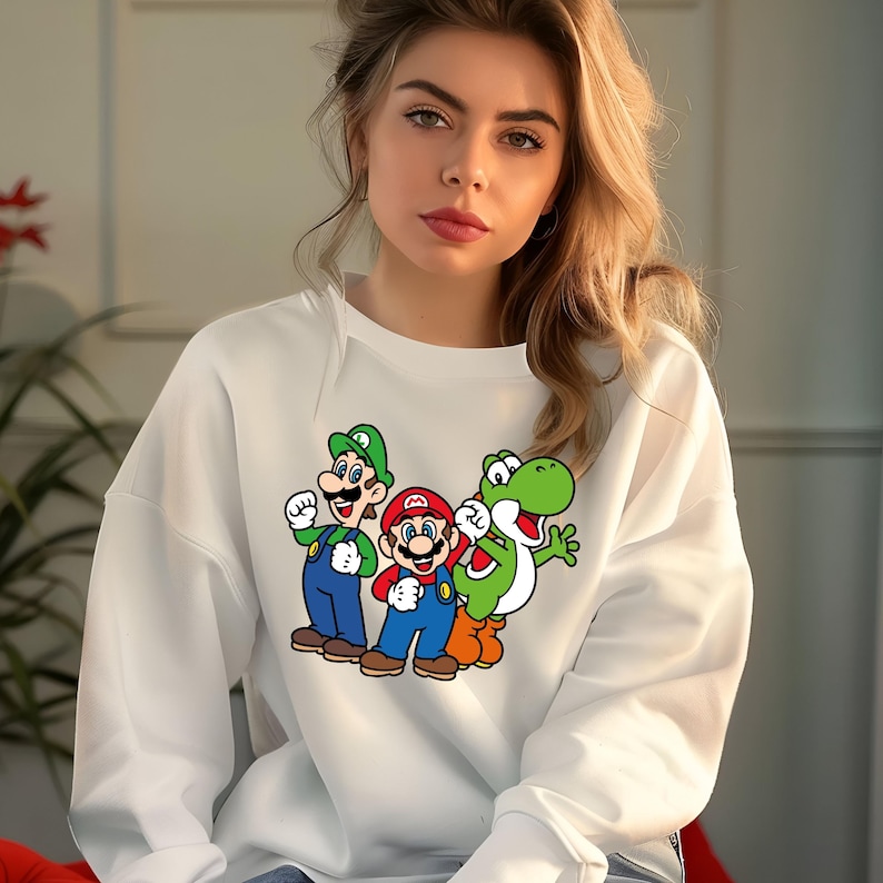 Pode incluir: Camisola branca com um gr&aacute;fico colorido de Mario, Luigi e Yoshi. As personagens de desenhos animados usam seus trajes caracter&iacute;sticos: vermelho, verde, azul e laranja. A camisola &eacute; de estilo casual e confort&aacute;vel.