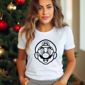 Pode incluir: Camiseta branca com um gr&aacute;fico em preto e branco do personagem de videogame Mario. O design mostra o rosto de Mario, incluindo seu chap&eacute;u, bigode e express&atilde;o sorridente. A camiseta &eacute; de estilo gola redonda cl&aacute;ssica.