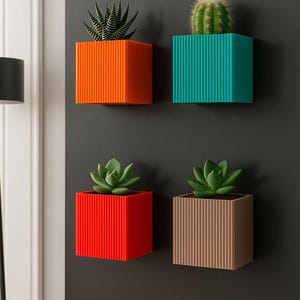 Può includere: Quattro fioriere quadrate colorate con texture a coste verticali, ognuna con una diversa succulenta o cactus. Le fioriere sono arancioni, verde acqua, rosse e marroni. Sono montate su una superficie grigio scuro.