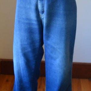 May include: Blue denim jeans with a high waist and flared leg. The jeans are displayed on a mannequin. The denim has a medium wash with some fading and a classic five-pocket design.