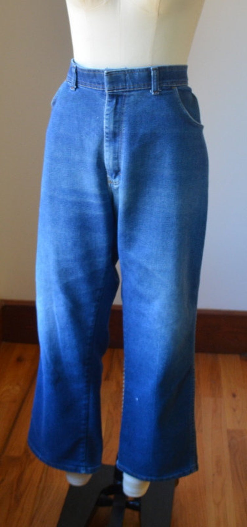 May include: Blue denim jeans with a high waist and flared leg. The jeans are displayed on a mannequin. The denim has a medium wash with some fading and a classic five-pocket design.