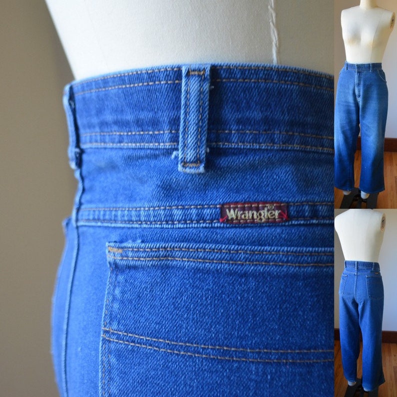 May include: Blue denim Wrangler jeans with a high waist and straight leg. The jeans feature a red Wrangler label on the back pocket and contrasting tan stitching. The jeans are displayed on a mannequin.