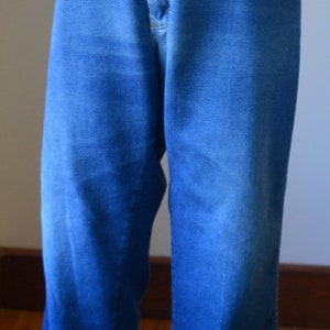 May include: Blue denim jeans with a high waist and flared legs. The jeans are displayed on a mannequin, showcasing the classic design and fit. The fabric has a slight fade, adding to the vintage aesthetic.