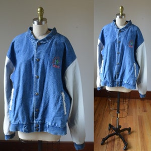 Può includere: Giacca di jeans blu con maniche bianche e chiusura con bottoni. La giacca presenta un design ricamato con la scritta "DRT" e un cactus. La giacca è esposta su un manichino.