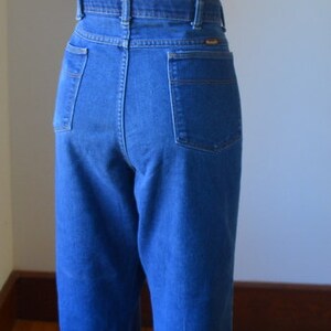May include: Blue denim jeans with a high waist and straight leg. The jeans have pockets on the front and back, and are displayed on a mannequin. The jeans are a medium wash and have a classic, timeless style.