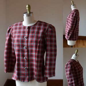 以下が含まれることがあります： 丸いネックラインと七分袖の、赤、黒、グレーのチェック柄のヴィンテージブレザー。 ブレザーはスカラップの裾で、黒いボタンで留められています。 衣類はマネキンに展示されています。