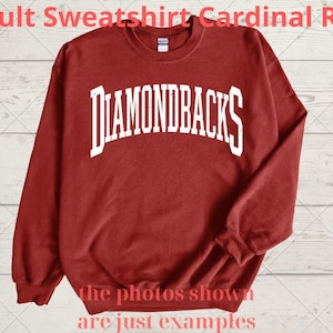 May include: Cardinal red adult sweatshirt with the word "DIAMONDBACKS" in white block letters across the chest. The sweatshirt has long sleeves and a crew neck. The text "the photos shown are just examples" is at the bottom.