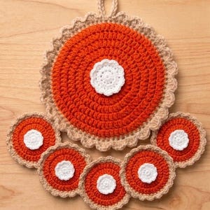 May include: A large circular orange crochet potholder with a white central flower and a beige scalloped border, accompanied by five smaller matching circular orange crochet coasters, each featuring a white central flower and a beige scalloped edge.