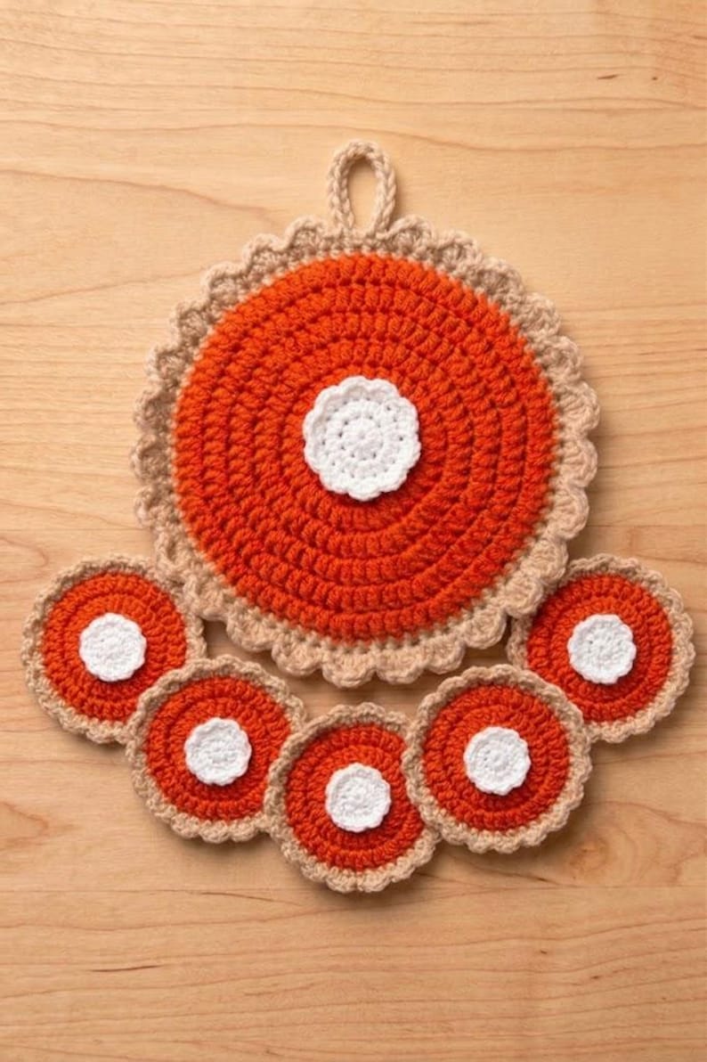 May include: A large circular orange crochet potholder with a white central flower and a beige scalloped border, accompanied by five smaller matching circular orange crochet coasters, each featuring a white central flower and a beige scalloped edge.