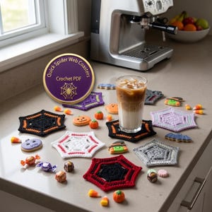 May include: A collection of hexagonal crochet spider web coasters in black, white, red, purple, and gray. A glass of iced coffee sits on a black coaster. Scattered Halloween-themed cookies and candies surround the coasters on the counter.