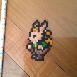 May include: A white pencil with a silver eraser and a pixel art figure of a character with brown hair, a green shirt, and a brown basket. The pencil is decorated with colorful hearts and bows.
