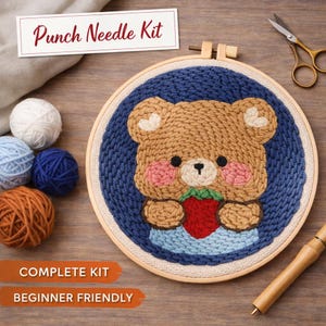 May include: Punch needle kit featuring a brown bear holding a red strawberry, surrounded by a blue background. The kit includes yarn balls in various colors, a wooden embroidery hoop, and the text "Punch Needle Kit", "Complete Kit", and "Beginner Friendly".