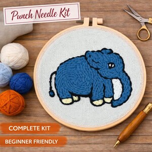Peut inclure: Un kit de punch needle complet avec un motif d'éléphant bleu. Le kit comprend un cercle à broder en bois, des échevettes de laine de différentes couleurs et des ciseaux. Le texte "Punch Needle Kit", "Complete Kit" et "Beginner Friendly" est visible.