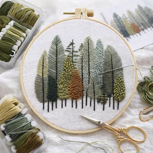 May include: An embroidery hoop with a forest scene stitched in various shades of green, brown, and gray thread. The design features detailed trees with textured surfaces. Embroidery floss and gold scissors are visible.