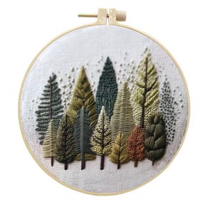 Puede incluir: Escena de bosque bordada en un aro de madera redondo. La obra presenta una variedad de &aacute;rboles en tonos verdes, marrones y dorados, con puntadas detalladas que crean textura y profundidad. El fondo es de tela clara.