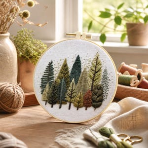 Puede incluir: Un bordado de una escena de bosque en un aro de madera redondo. La obra de arte presenta varios tonos de verde, marr&oacute;n y dorado, que representan una colecci&oacute;n de &aacute;rboles estilizados. El fondo es de tela clara.