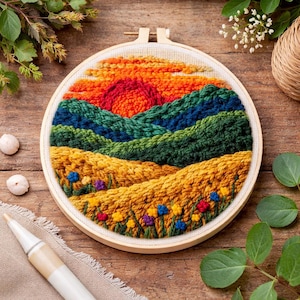 Könnte beinhalten: Handgefertigtes Stickrahmen-Kunstwerk mit einem Sonnenuntergang über sanften Hügeln. Das Kunstwerk verwendet leuchtende Farben wie Orange, Rot, Grün, Blau und Gelb, mit detaillierten Texturen und kleinen floralen Akzenten. Das Stück ist in einem Holzrahmen gefasst.