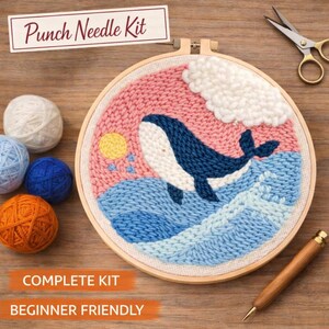 May include: A punch needle kit with a whale design. The artwork features a blue whale in the ocean with a pink sky, yellow sun, and white cloud. The kit includes yarn balls, a wooden hoop, scissors, and a punch needle tool. Text reads "Punch Needle Kit", "Complete Kit", and "Beginner Friendly".