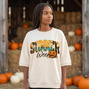 Op de afbeelding: Een crèmekleurig sweatshirt met ronde hals en een grafische print met de tekst "SUMMER Ween". Het ontwerp toont een skelet dat ontspant in een hangmat op een strand, een palmboom en een pompoen tegen een achtergrond van een zonsondergang.