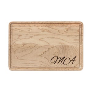 Op de afbeelding: Een rechthoekige houten snijplank met een sapgroef en afgeronde randen. De lichtgekleurde houtnerf is zichtbaar. De initialen "MCA" zijn elegant in cursiefschrift gegraveerd in de rechter benedenhoek.