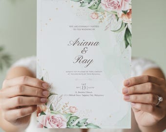Può includere: Un invito di nozze con composizioni floreali rosa e verdi. L'invito include i nomi "Ariana & Ray" e la data "SAT 15". È visibile anche il testo "Siete cordialmente invitati al matrimonio di".