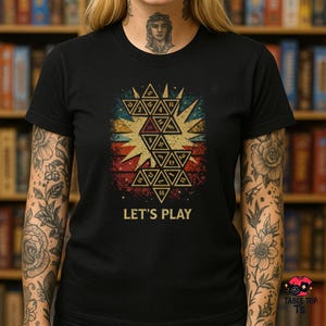 May include: Black t-shirt with a geometric design featuring numbers and the text "LET'S PLAY". The design uses red, yellow, and blue, with a vintage, distressed appearance. The shirt is from Table Top Ts.