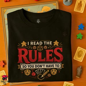 May include: Black t-shirt with the text "I READ THE RULES SO YOU DON'T HAVE TO" in red and white. The design includes dice, player figures, and a pencil. The shirt is folded on a wooden surface with game pieces.
