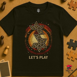 May include: Black t-shirt with a geometric design in orange, red, and yellow, featuring numbers and the text "LET'S PLAY." The shirt has a crew neck and short sleeves. The design is centered on the chest.