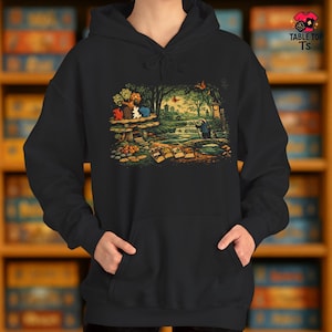 May include: Black hoodie with a vibrant forest scene illustration. The design shows a bridge, waterfall, and several creatures. The text "TABLE TOP TS" is visible in the top right corner of the design.
